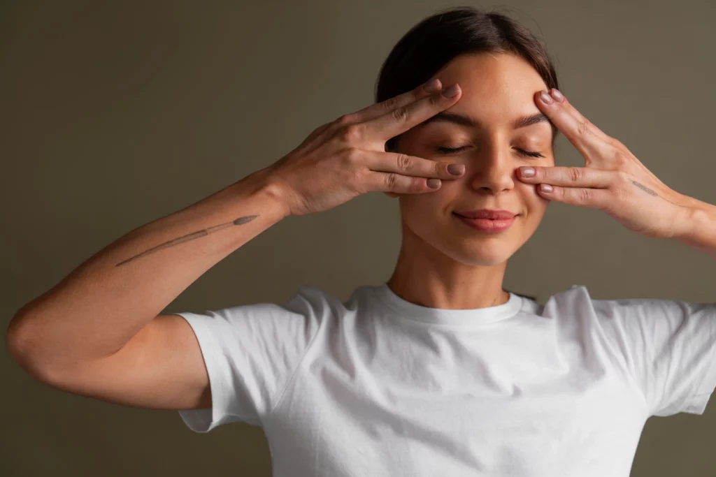 Woman practicing face yoga with eyes closed, gently pressing fingers around her eyes to tone facial muscles and promote relaxation through natural face yoga techniques.