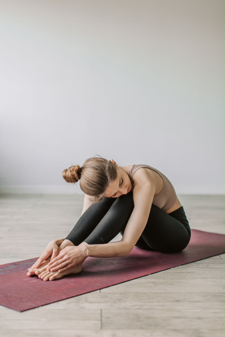 Woman in a seated forward fold on a yoga mat in a bright, quiet room