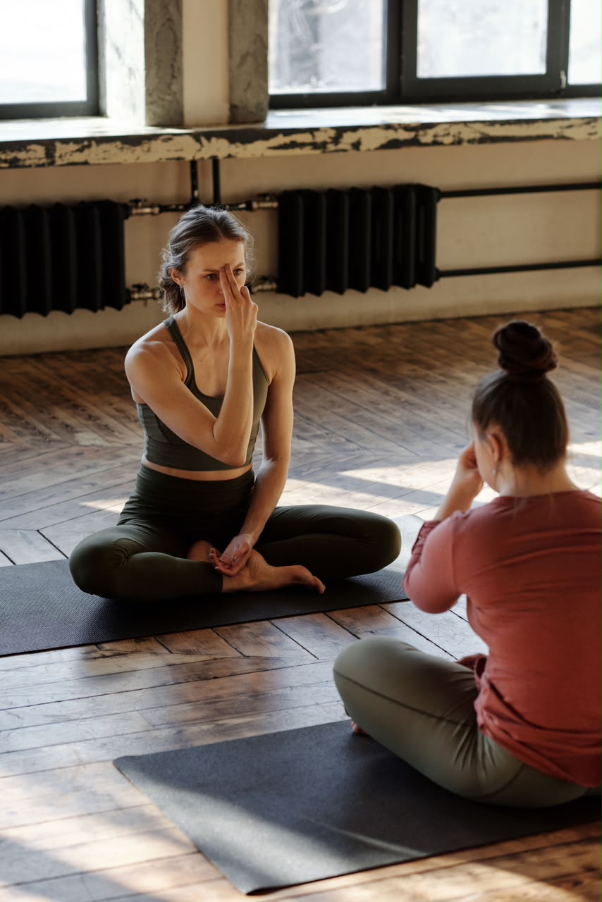 Yoga instructor guiding a student through a breathing technique, both seated on mats